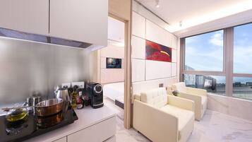 Una habitación de hotel moderna con cocina, un ventanal con vistas y una zona de estar con sofá y sillones.