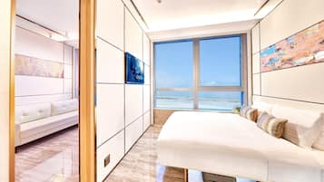 A modern bedroom with a large bed, a seating area, and a view of the ocean.