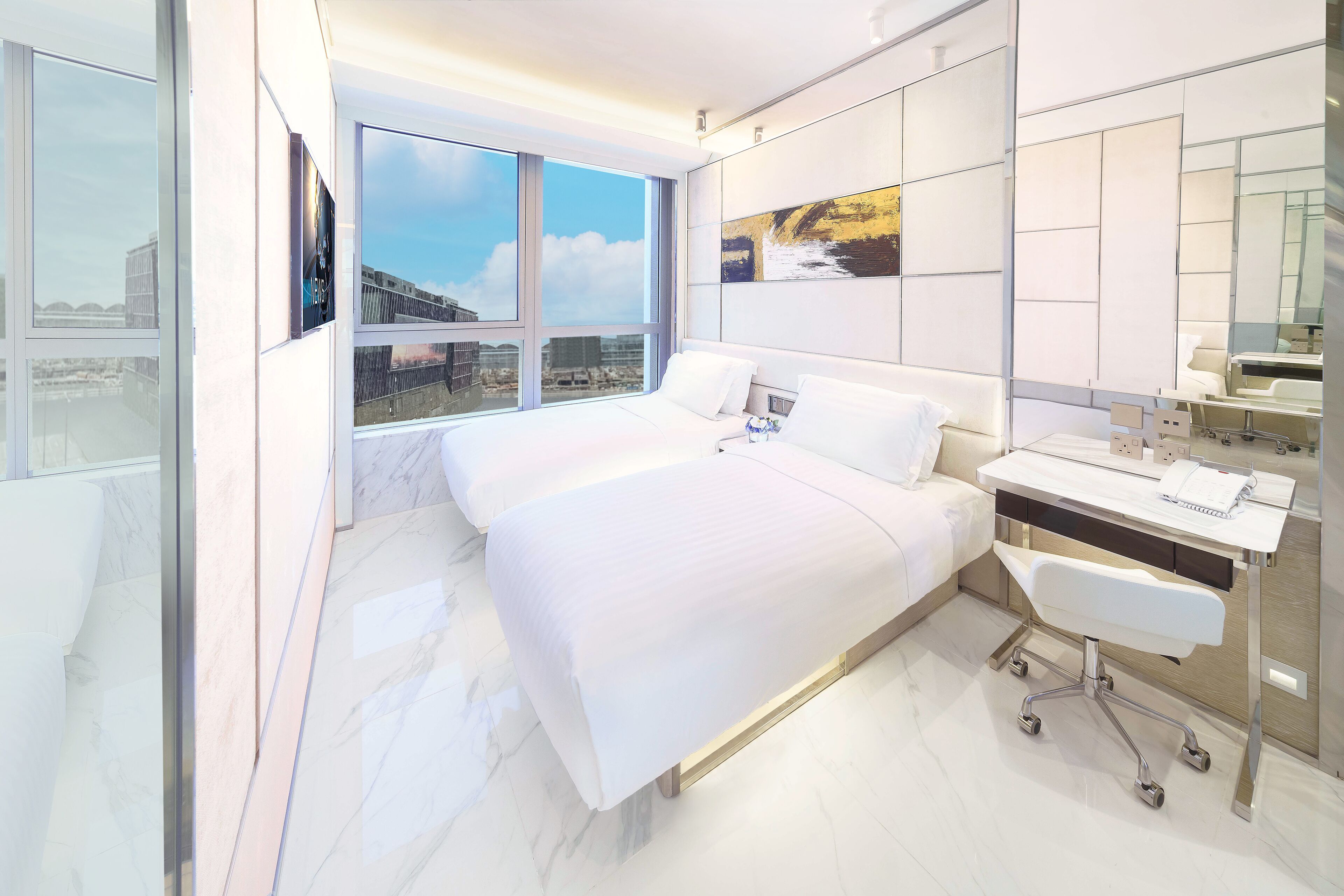 A modern hotel room with a large bed, a desk, and a view of the city.