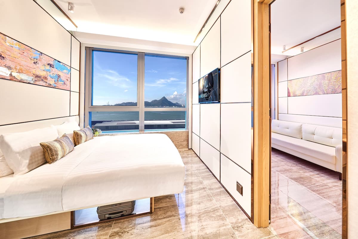 Ein modernes Schlafzimmer mit einem großen Bett, einer Couch und Blick auf ein Gewässer und Berge.