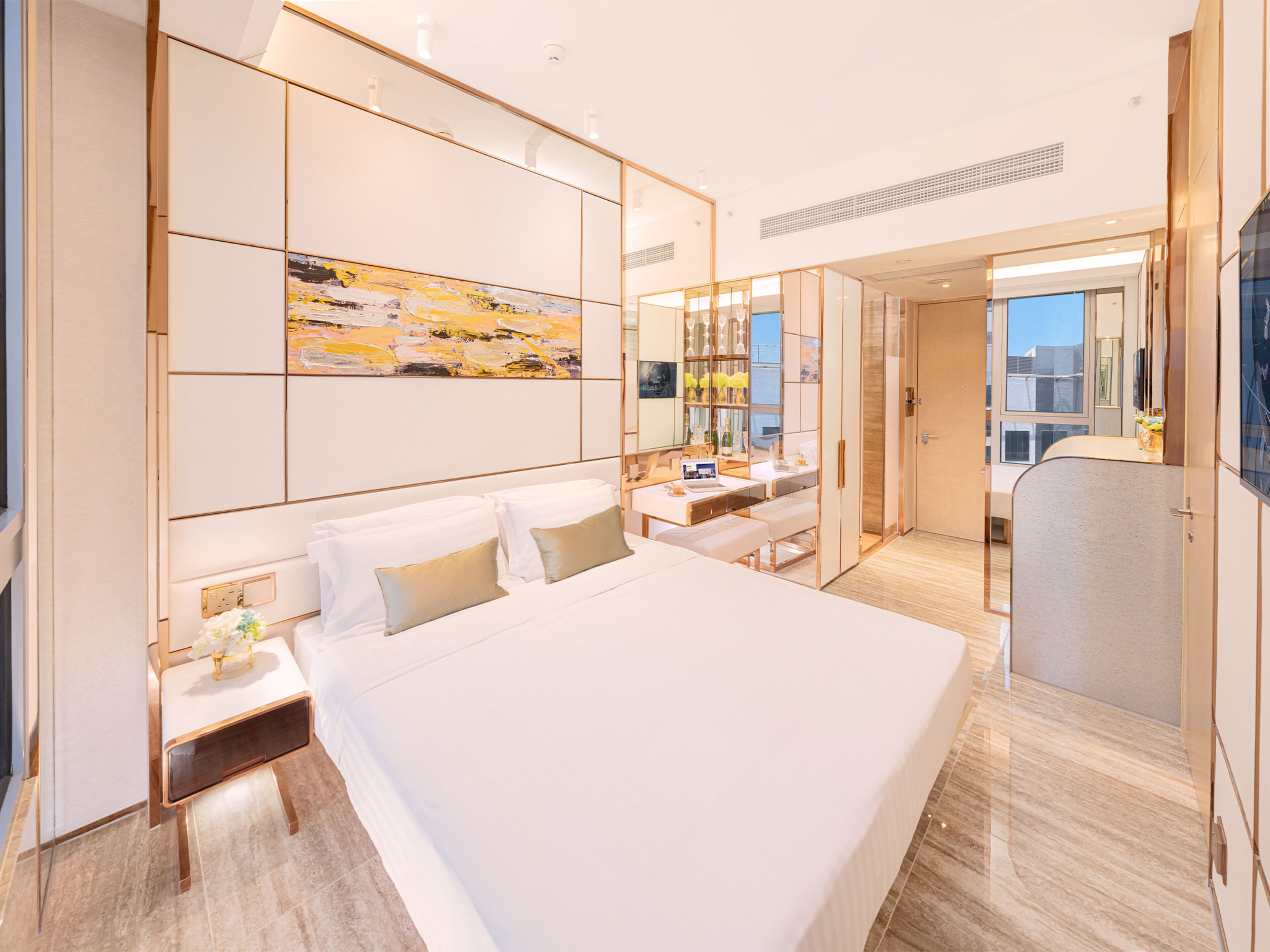 A modern hotel room with a large bed, a desk, a vanity, and a large window.