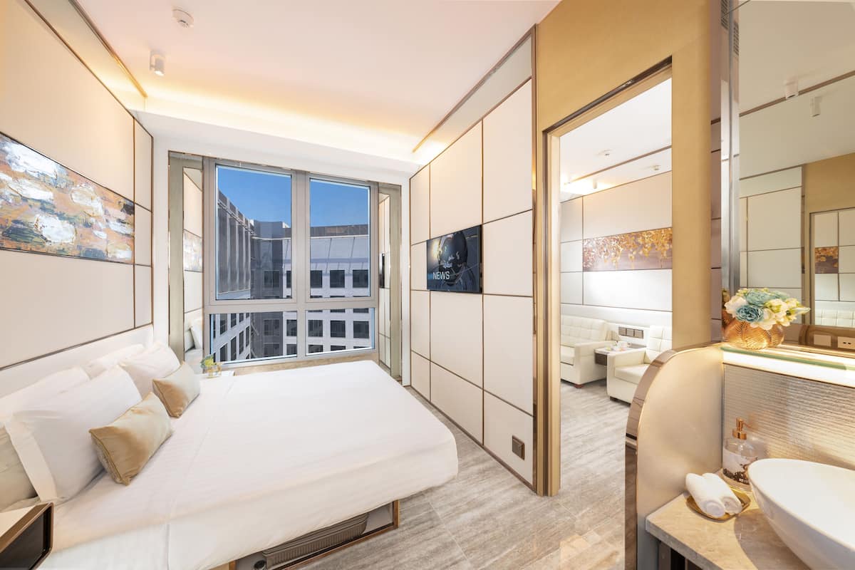 Ein modernes Hotelzimmer mit einem großen Bett, einer Sitzecke, einem Badezimmer mit großem Spiegel und Blick auf die Stadt durch das Fenster.