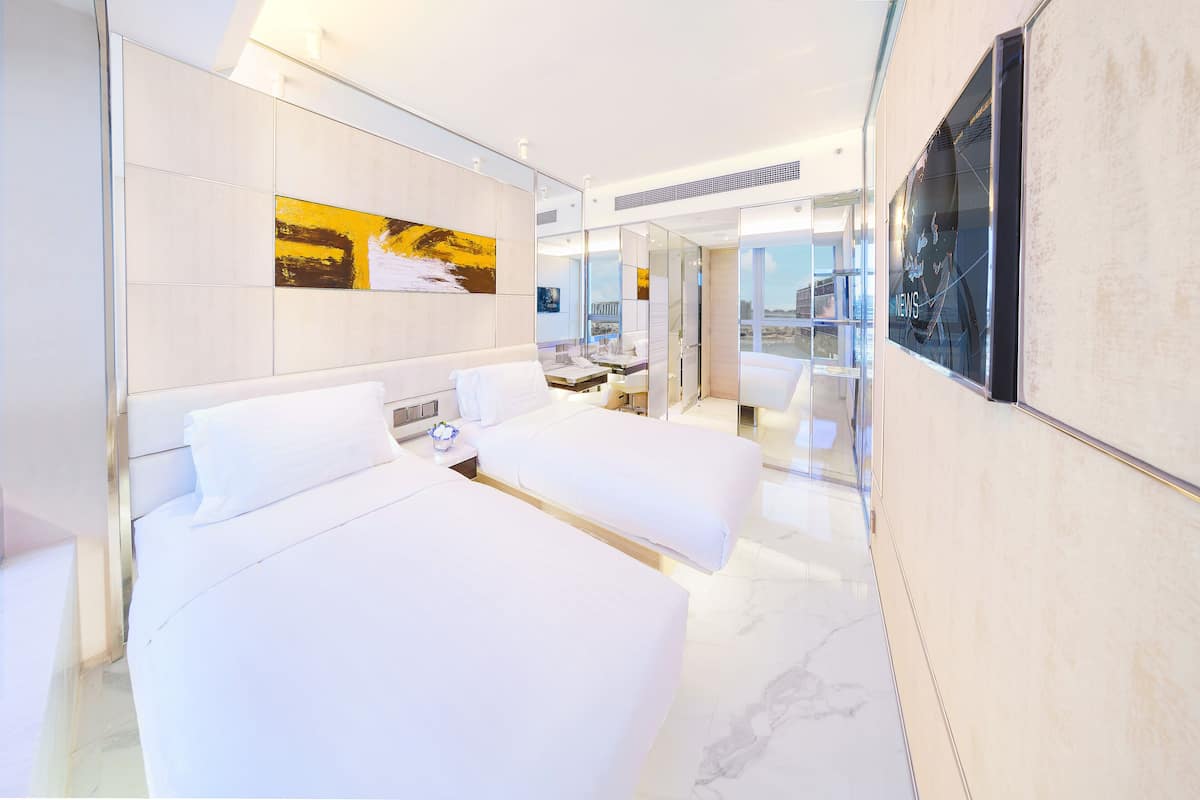 Ein modernes Hotelzimmer mit zwei Betten, einem großen Spiegel und Blick auf die Stadt.