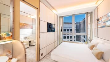 A modern hotel room with a large bed, a sitting area with a sofa, a bathroom with a sink and mirror, and a large window offering a city view.
