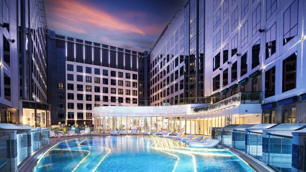 Un hotel moderno con una amplia piscina interior, varios pisos y fachada de vidrio.