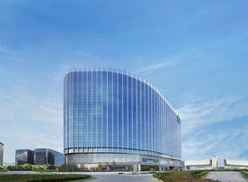 A modern, curved glass building with a prominent entrance and a landscaped area in front.