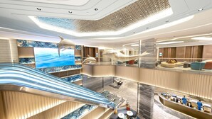 Un moderno vestíbulo de hotel con una escalera central, zonas de descanso y una gran pantalla digital.