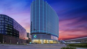 Un hotel moderno con fachada de vidrio curva, un logotipo destacado en la entrada y una zona de recepción bien iluminada.