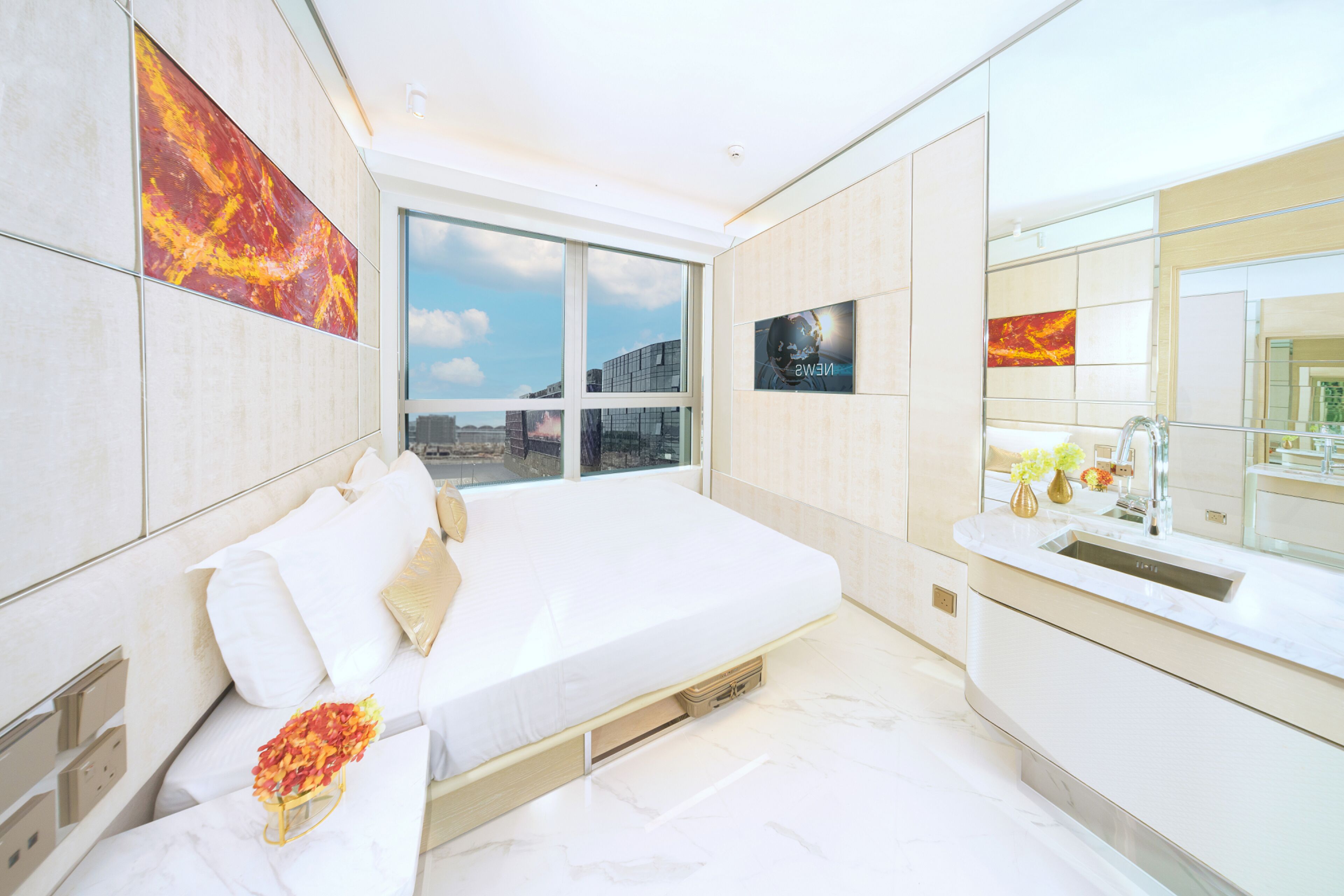 Un dormitorio moderno con una cama grande, un ventanal con vistas a la ciudad, un baño con lavamanos y espejo, y obras de arte en las paredes.