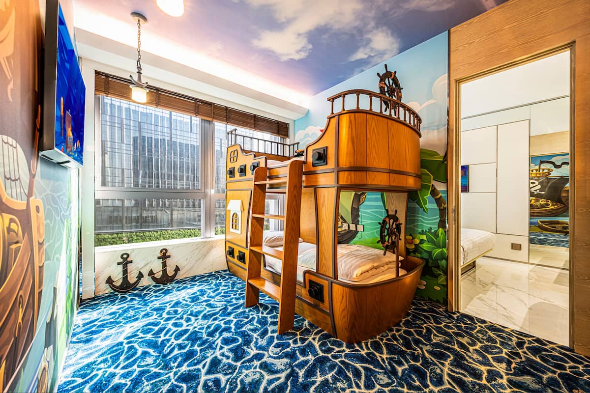 Ein Kinderstockbett mit Schiffsdesign, ein großes Fenster mit Jalousien und ein Wandgemälde eines Schiffes.