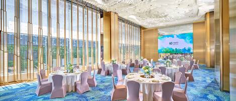 A spacious conference room with round tables, pink chairs, and a large screen displaying a hotel name.