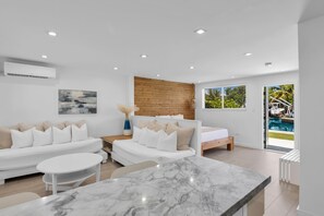 Una sala de estar moderna y bien iluminada con un sofá blanco, una mesa de centro de mármol y una pared de acento de madera.