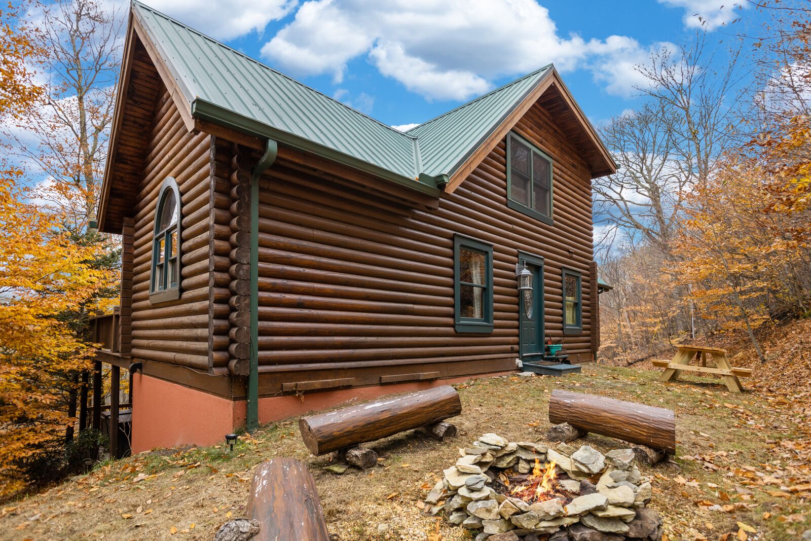 A log cabin with a stone fire pit and a picnic table in the yard.