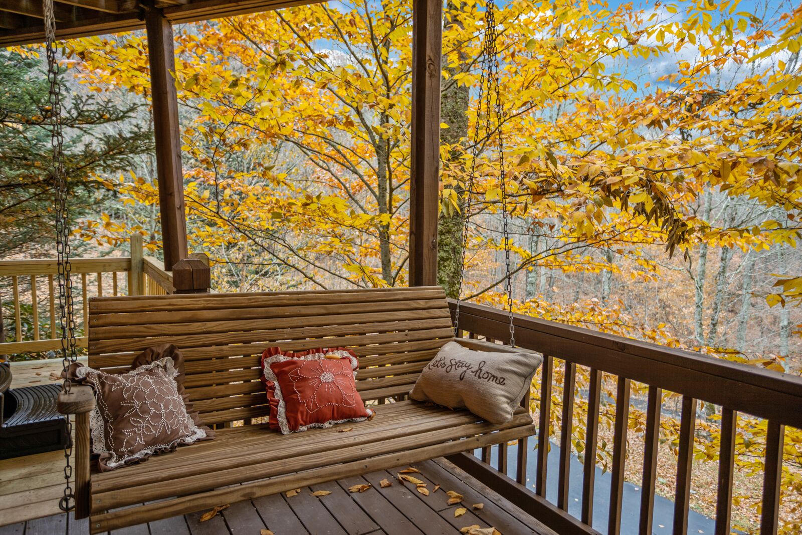 Un banco de madera con cojines sobre una terraza de madera, con vistas a un bosque de follaje otoñal.