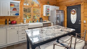 Eine Küche mit einer Marmorinsel, Holzschränken, einem Kühlschrank und einer schwarzen Tür mit einem dekorativen Kranz.