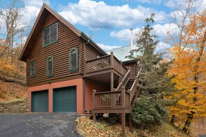 Eine Blockhütte mit einer zweistelligen Garage, einer überdachten Veranda und einer Treppe, die zu einer Terrasse führt.