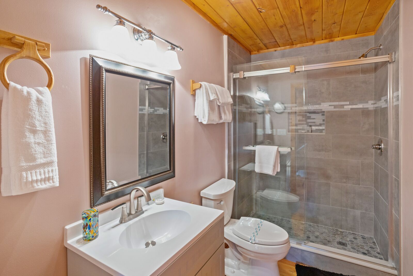 Een badkamer met een grote spiegel, een wit wastafelmeubel, toilet en een douche met glazen wanden.