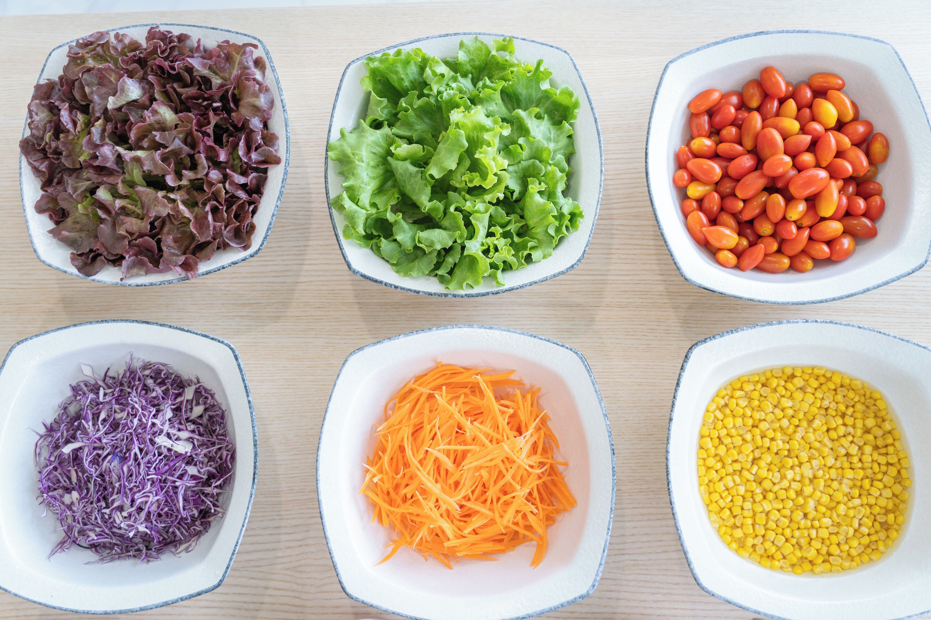 Tres tazones con distintos alimentos: repollo morado rallado, zanahorias naranjas ralladas y granos de maíz amarillo.