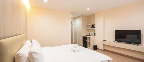 Quarto de hotel com uma cama, televisão fixada na parede e pequena área de cozinha.