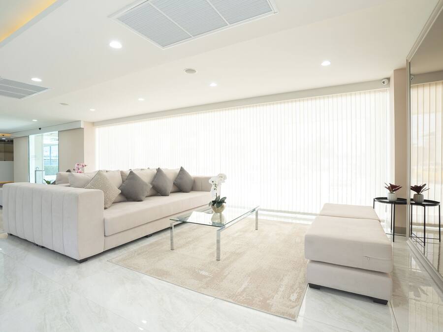 Een moderne woonkamer met een bank, poef, glazen salontafel en een groot raam met jaloezieën.
