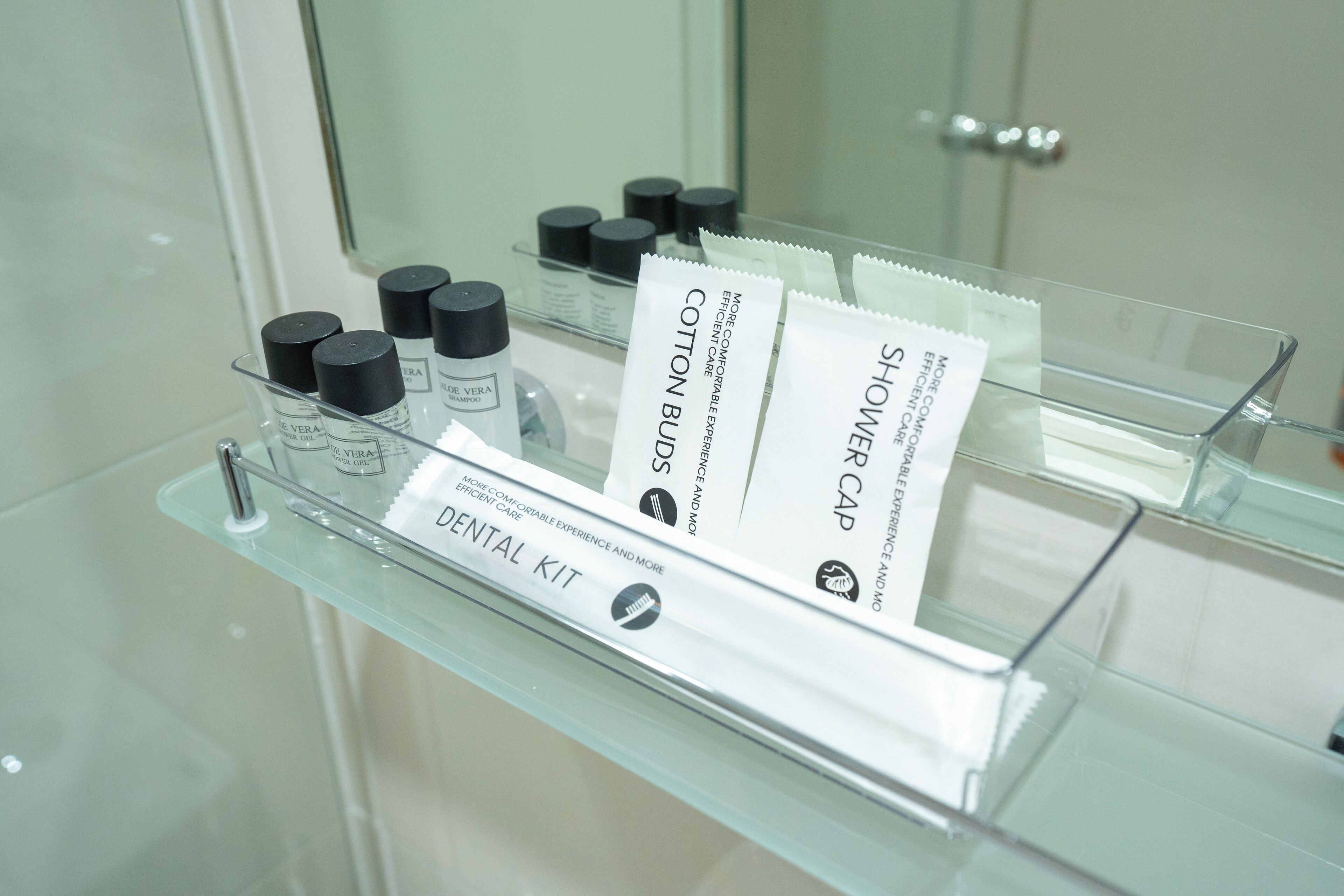 Un baño con repisas de vidrio que muestran un kit de tocador, bastoncillos de algodón y un gorro de ducha.