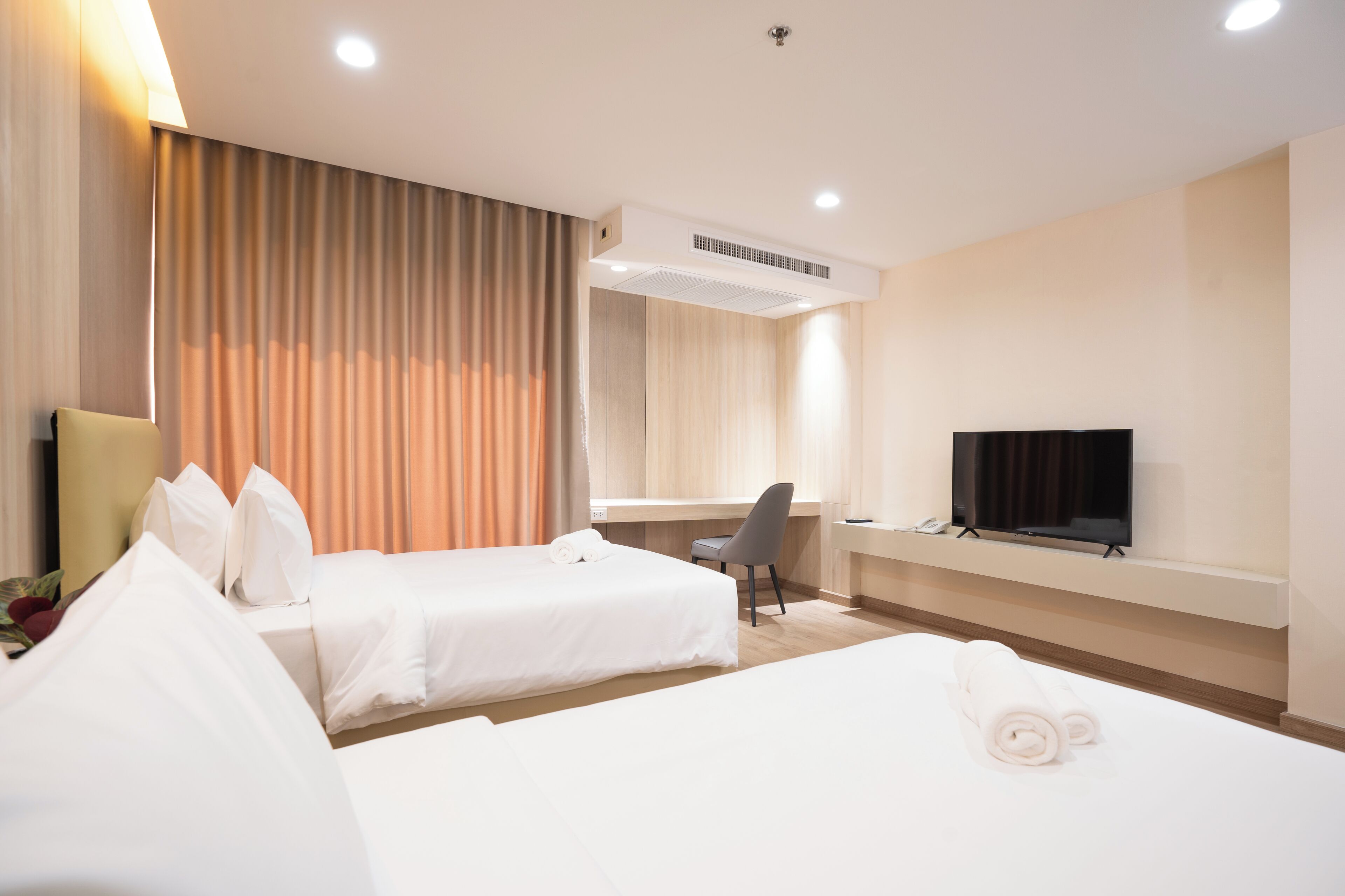 A hotel room with two beds, a desk, a chair, a TV, and an air conditioning unit.