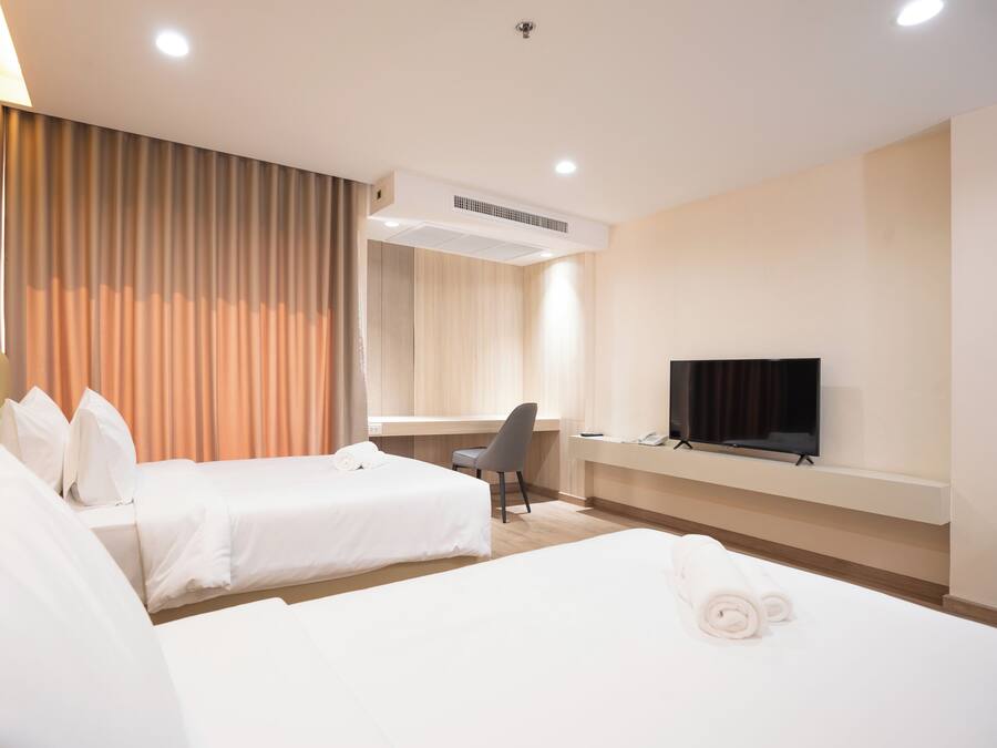 A hotel room with two beds, a desk, a chair, a TV, and an air conditioning unit.