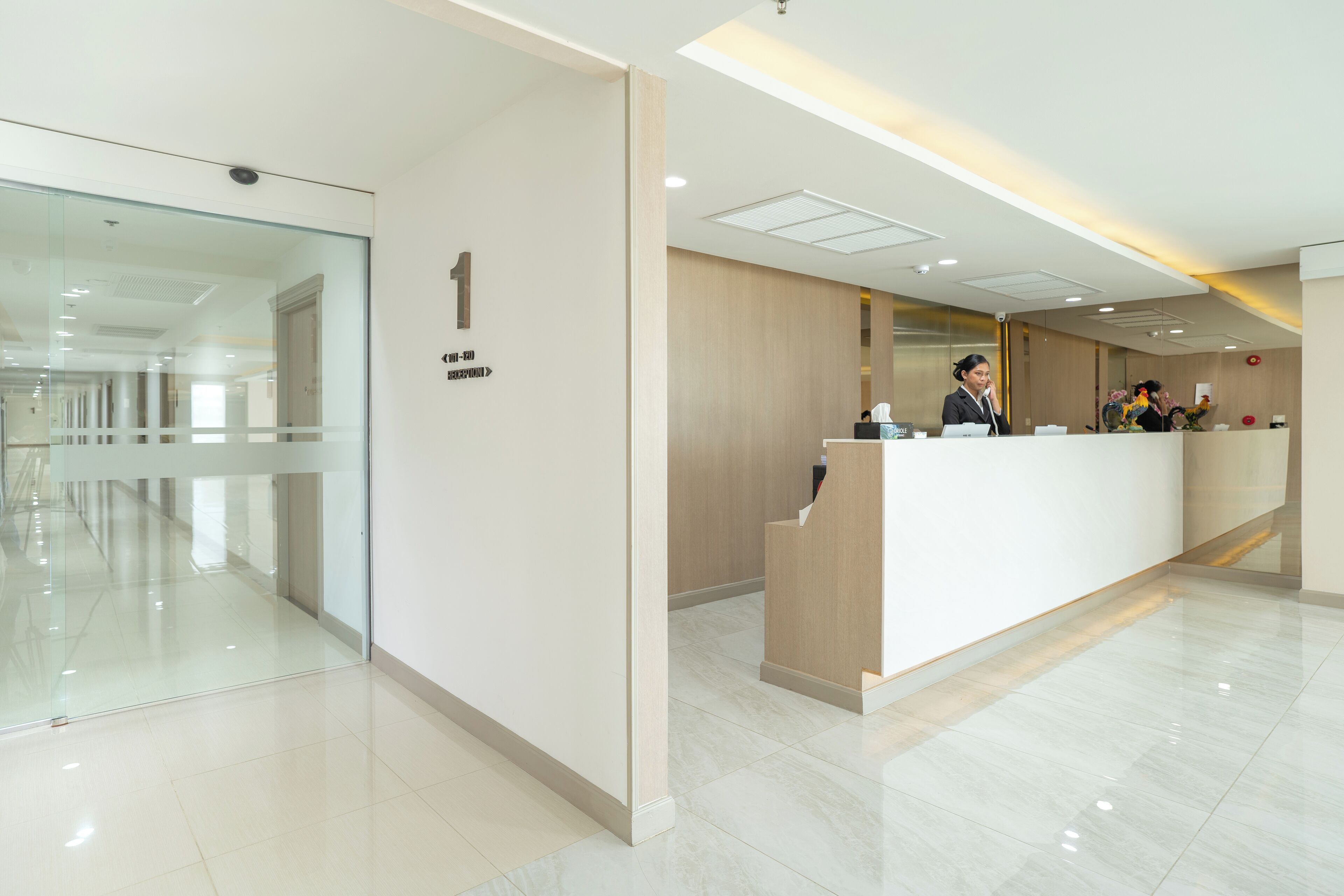 Una moderna área de recepción con un muro de cristal, un mostrador de recepción y un letrero que indica la habitación número 1.