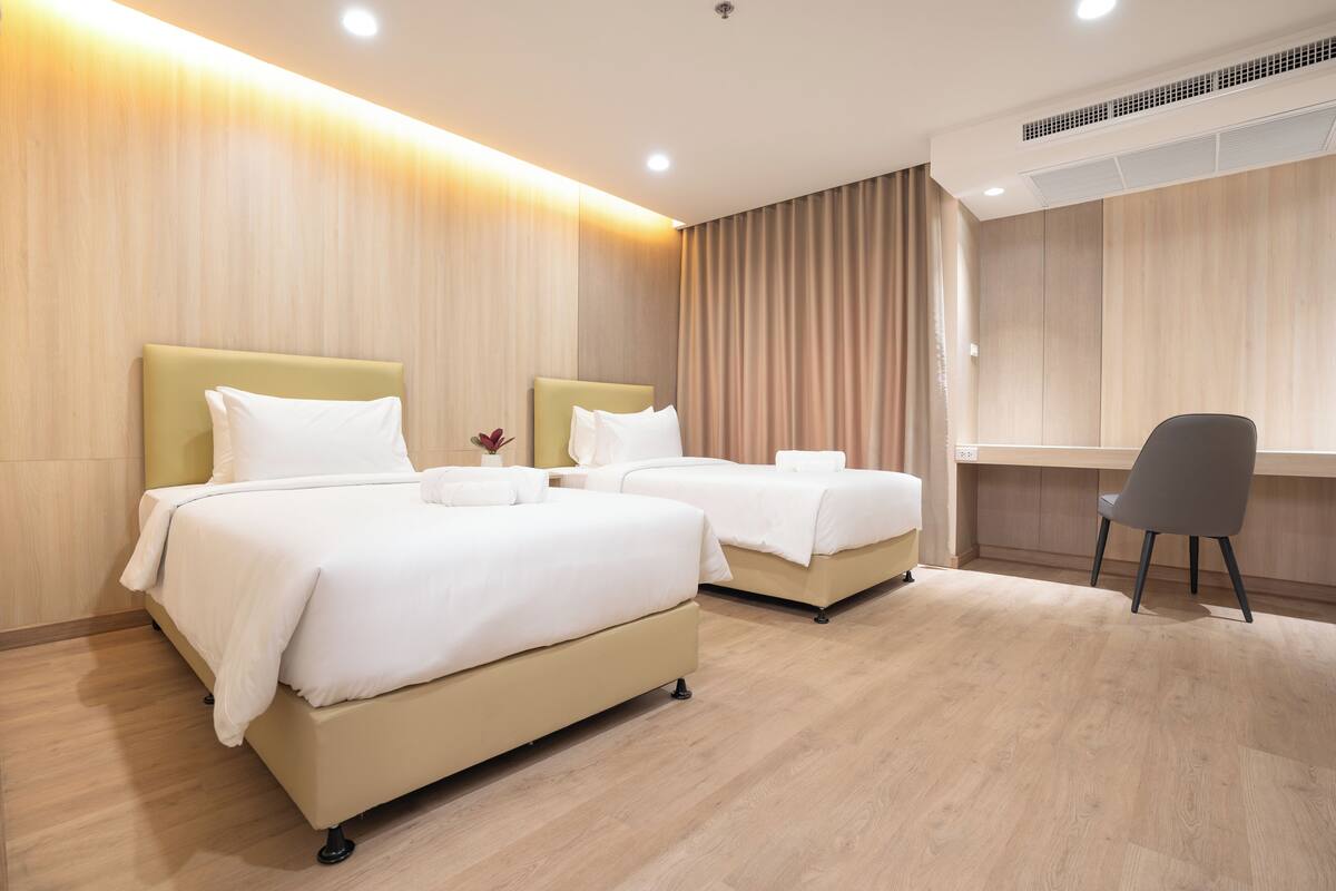 A hotel room with two beds, a desk, and an air conditioning unit.