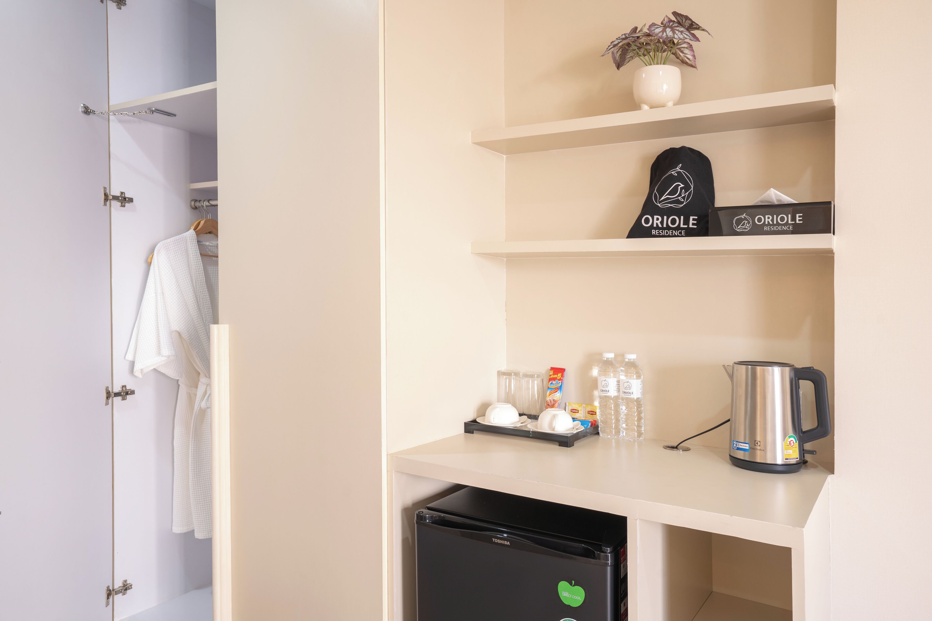 Habitación de hotel con minibar, refrigerador, cafetera, una planta y un perchero.