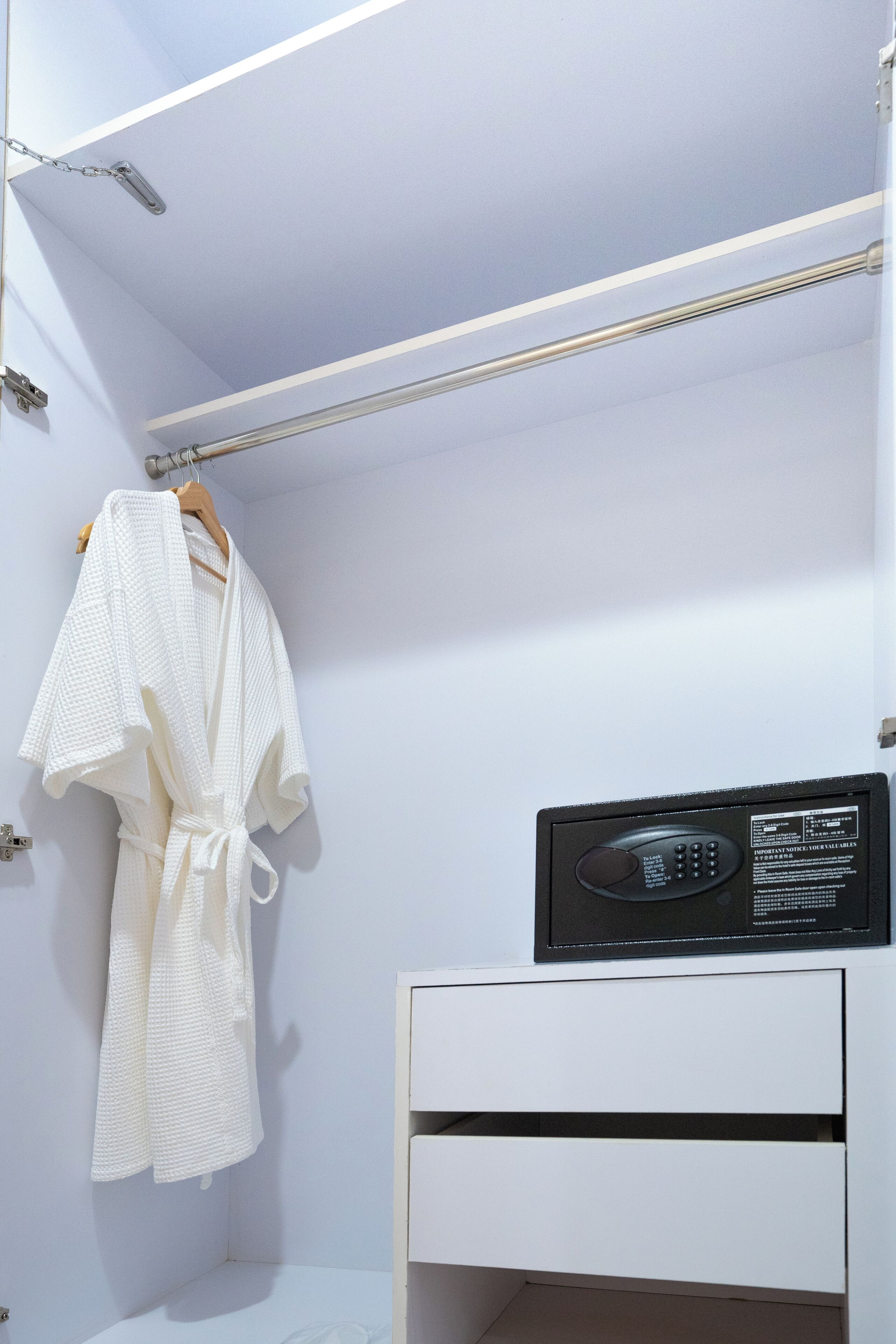 A white robe hanging on a rack, a black microwave on a white cabinet, and a white drawer below.