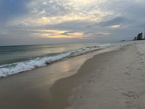 A beach with waves, a clear sky, and buildings in the distance. - 3BR Beach Condo Walk to Shops & Restaurants (Pensacola)
