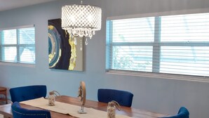 Zona pranzo con tavolo in legno, sedie imbottite blu, lampadario e un grande quadro astratto appeso al muro.