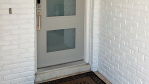 Facciata in mattoni bianchi con una porta grigia, un tappetino da porta con la scritta 'WELCOME' e una cassetta delle lettere nera.