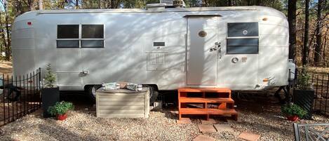 Una caravana estacionada con un pequeño porche, una cocina compacta y un espacio exterior cercado.