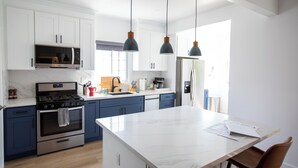 A modern kitchen with white cabinets, a central island, stainless steel appliances, and pendant lighting.