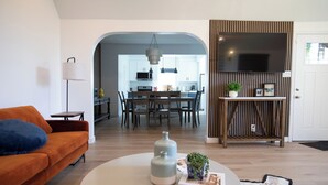 A modern living room with a sofa, a coffee table, and a dining area with a kitchen in the background.