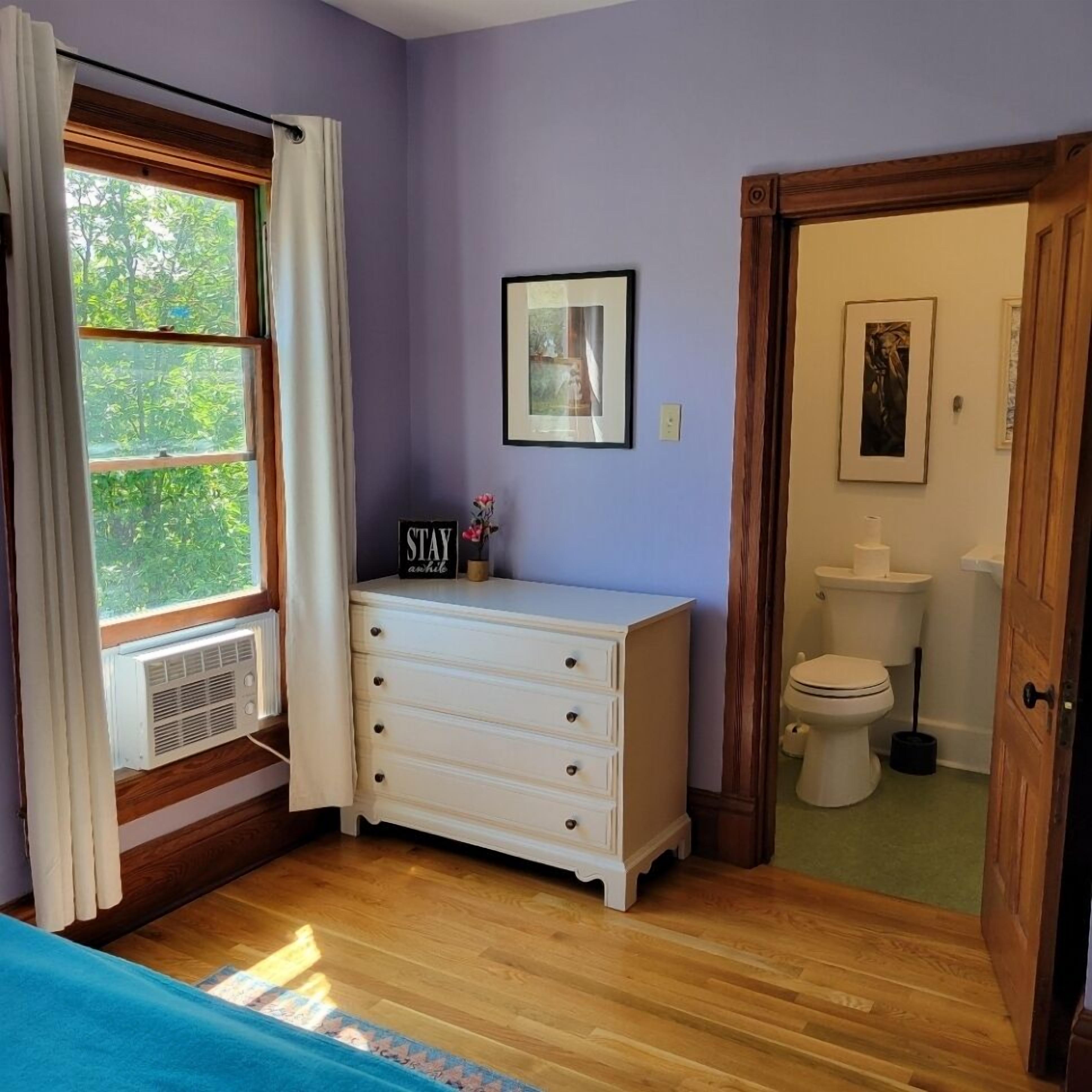 Ein Zimmer mit einem Holzkasten, einem gerahmten Bild und einem Fenster mit Vorhängen.