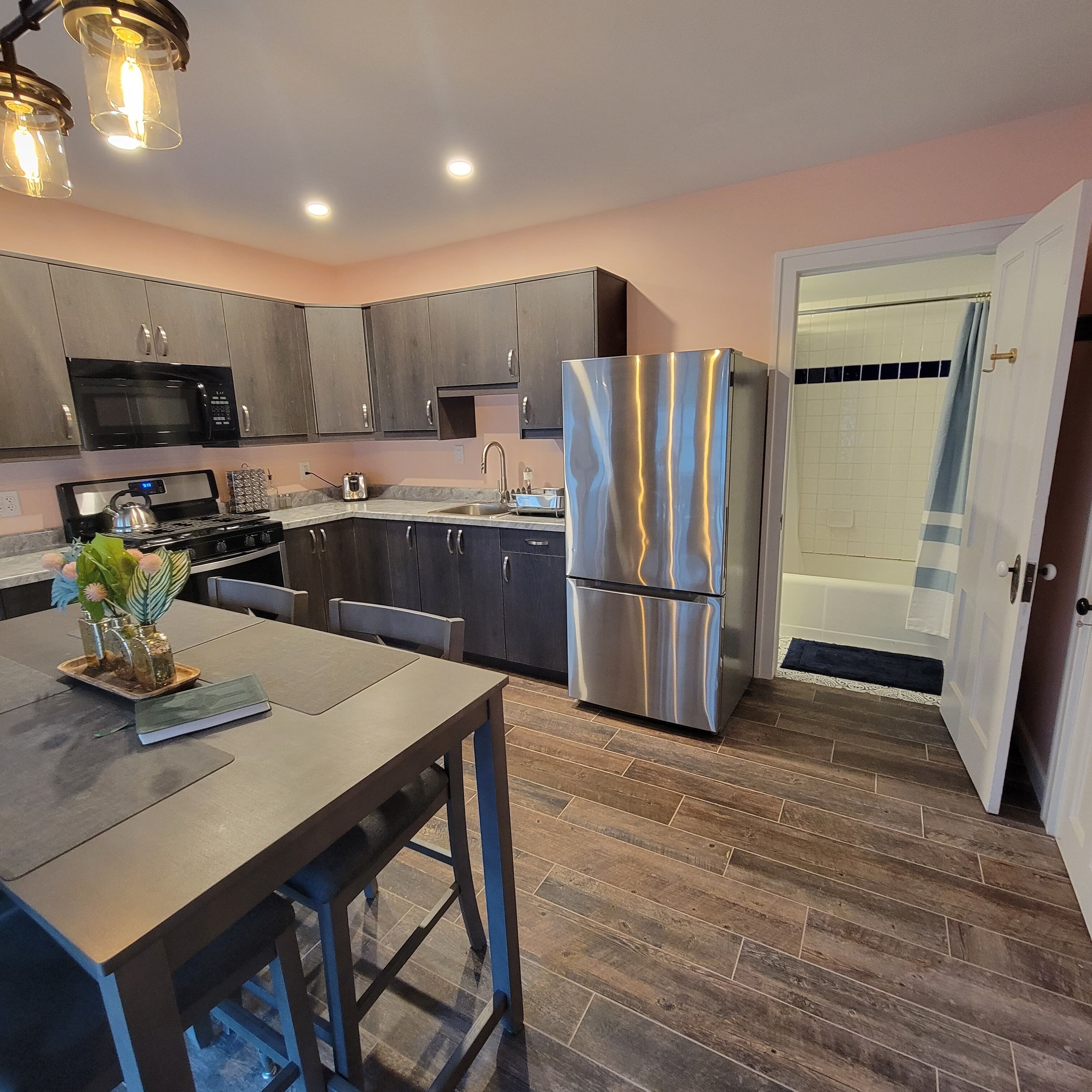 A modern kitchen with dark cabinets, stainless steel appliances, and a wooden dining table.