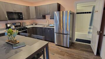 A modern kitchen with dark cabinets, stainless steel appliances, and a wooden dining table.