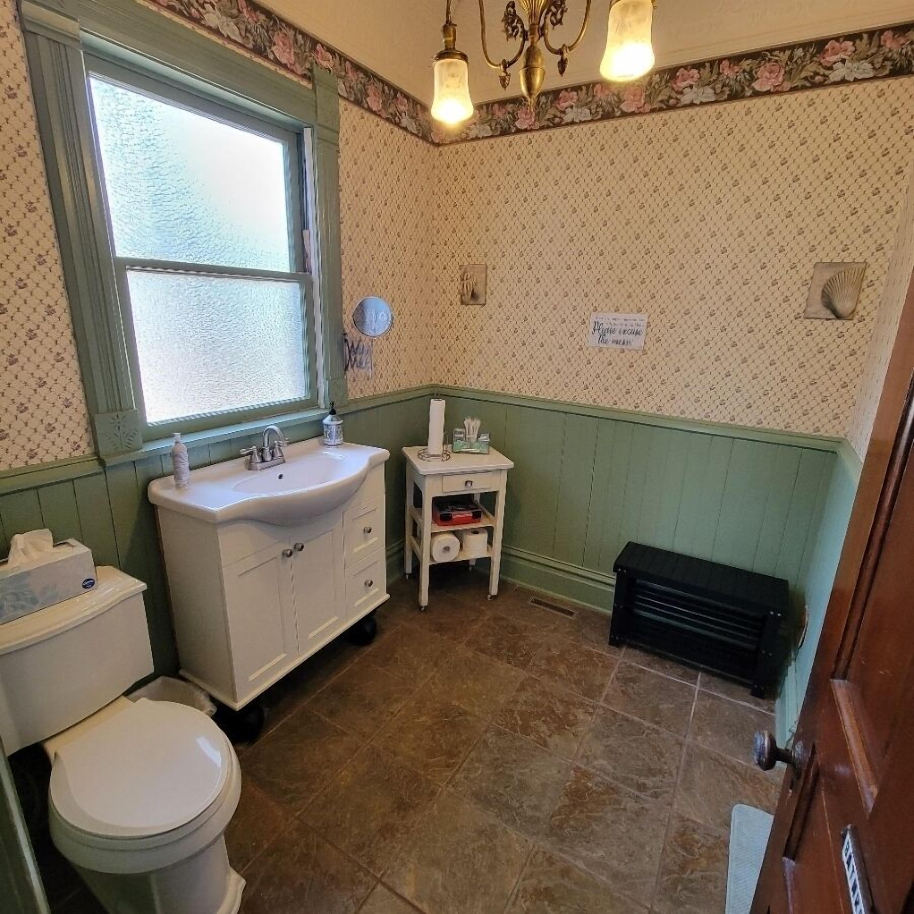 A bathroom with a toilet, sink, and window.