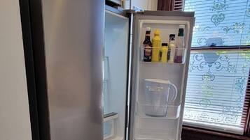Eine Küche mit einem Edelstahl-Kühlschrank, einer eingebauten Mikrowelle und einem Fenster mit Jalousien.