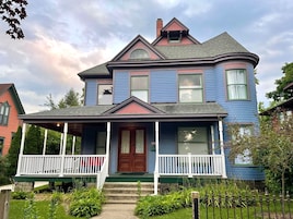 A two-story house with a porch, a chimney, and a large window.
