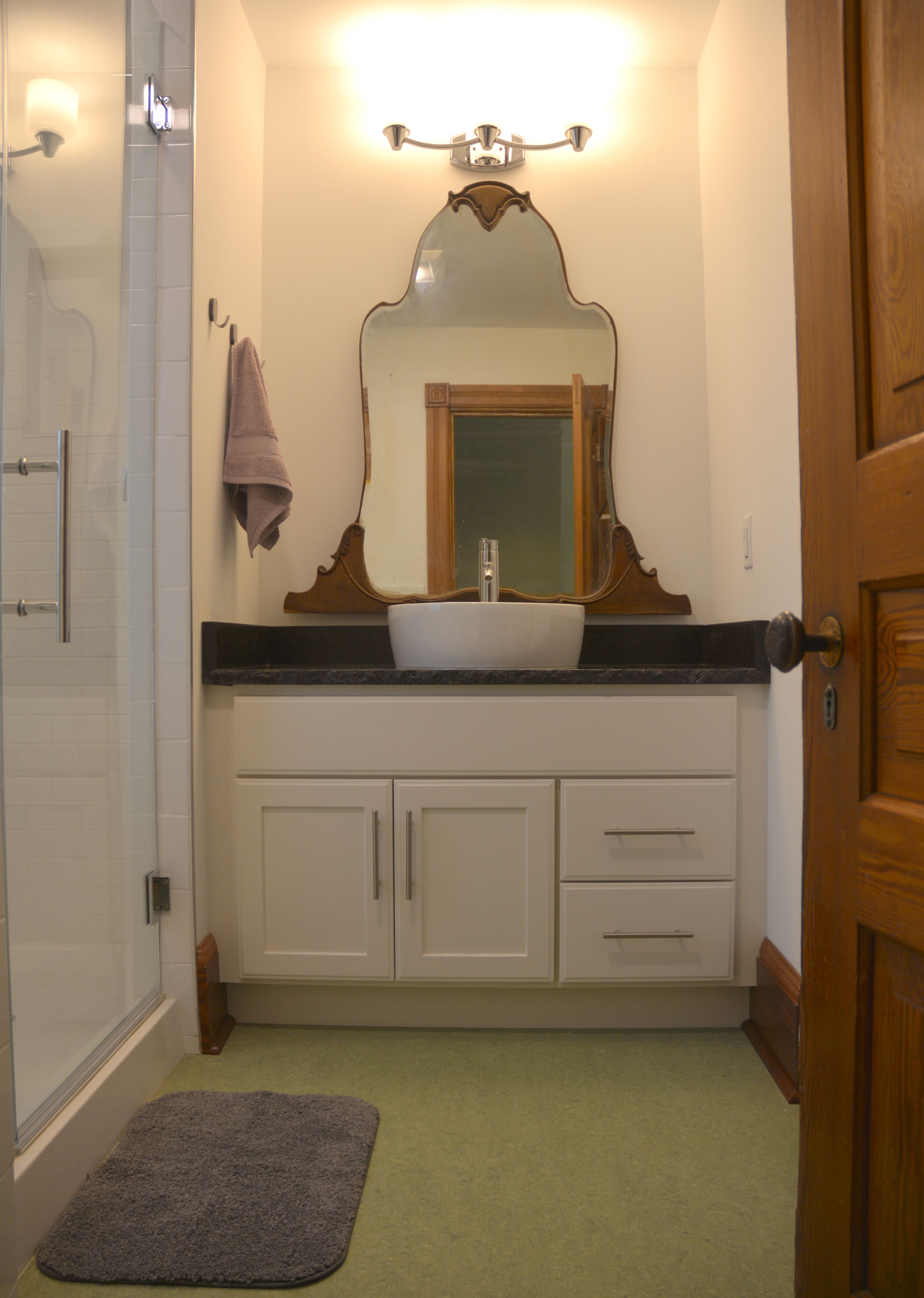 Een badkamer met een witte wastafel, een spiegel erboven en een douchedeur.