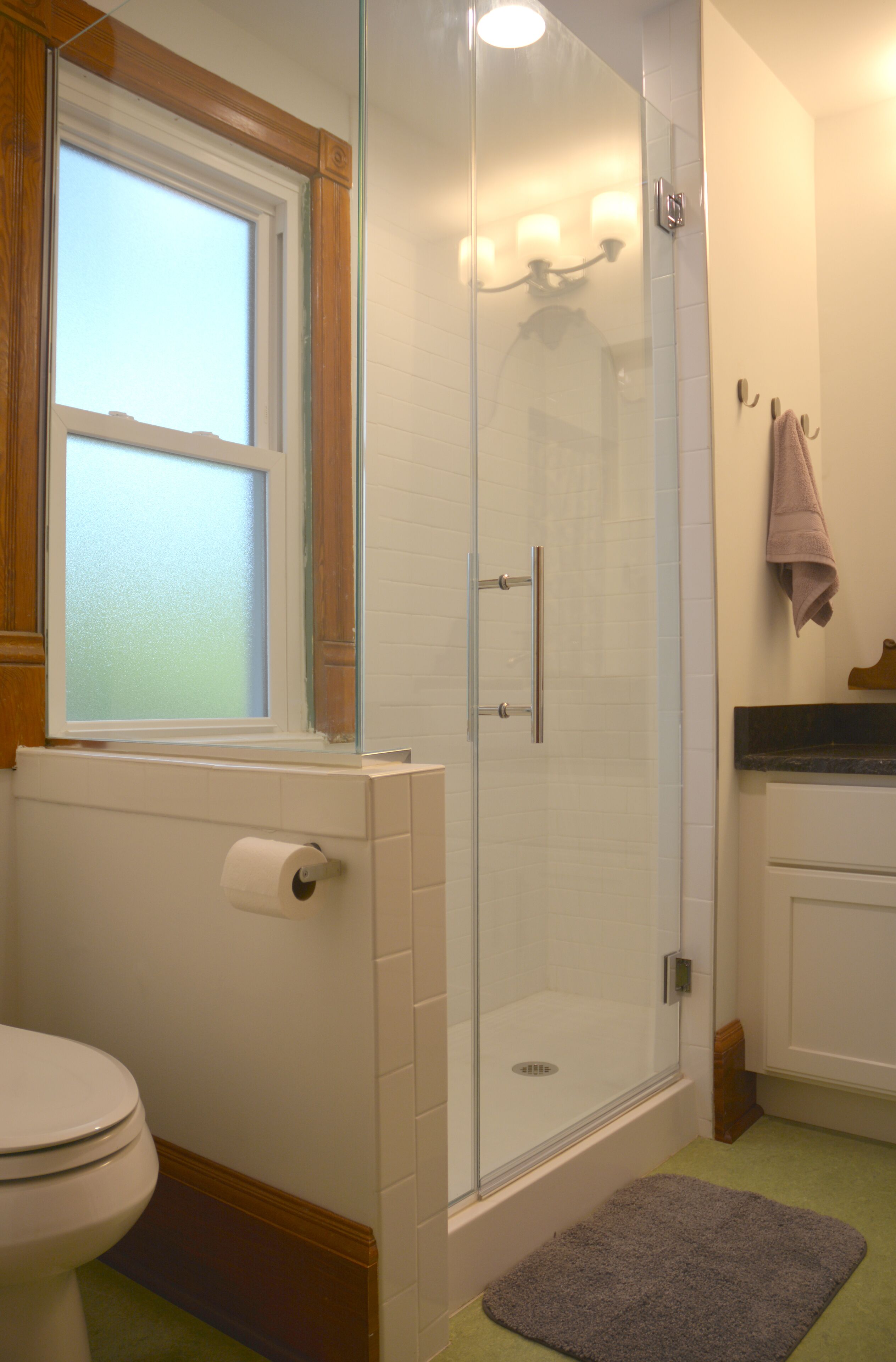 Een badkamer met een douchecabine van glas, een toilet en een raam.