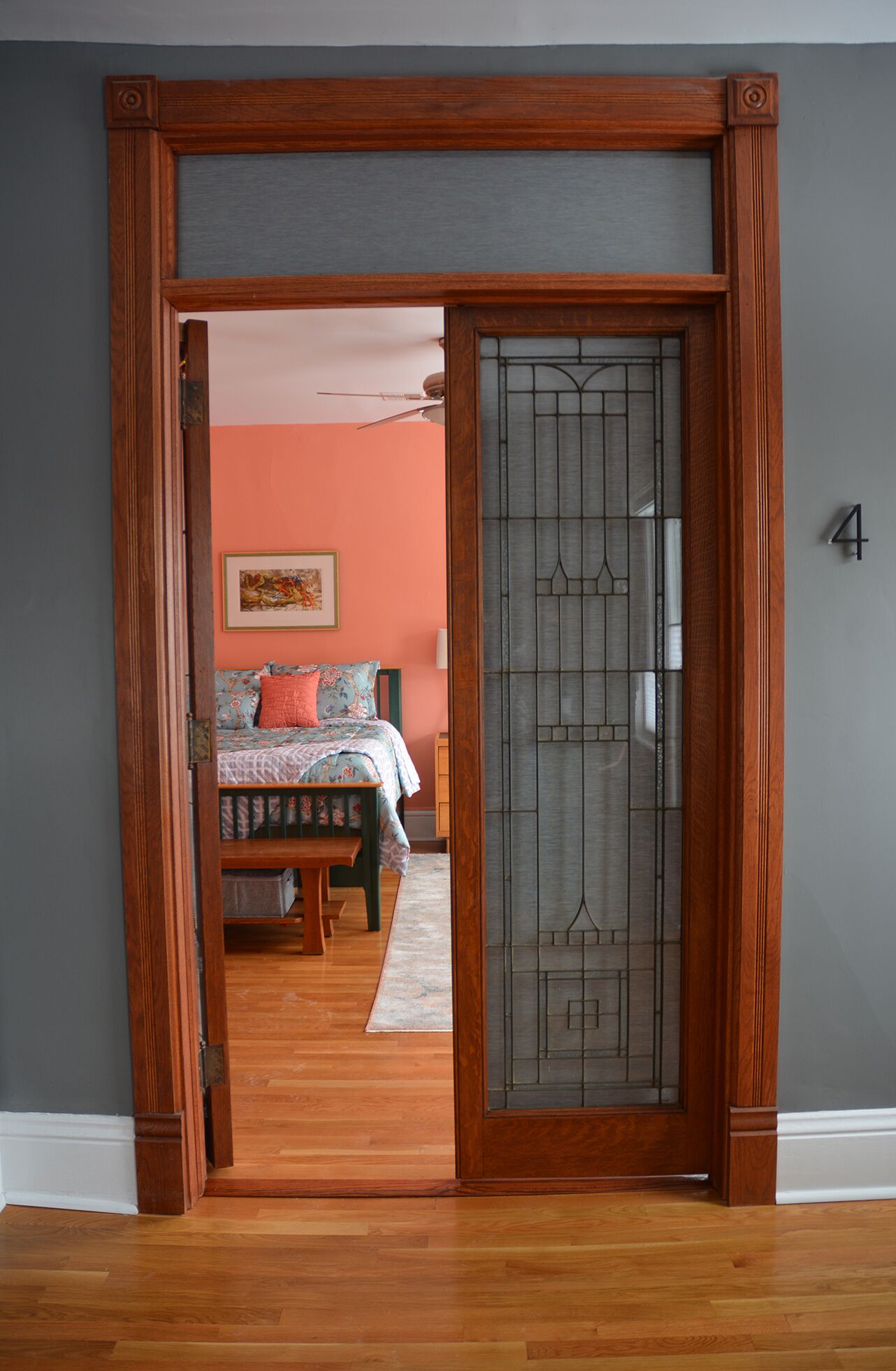 Une pièce dotée d’une porte à cadre en bois qui donne sur une chambre. La pièce a un mur gris, un plancher en bois et un lit avec une literie à motifs floraux.
