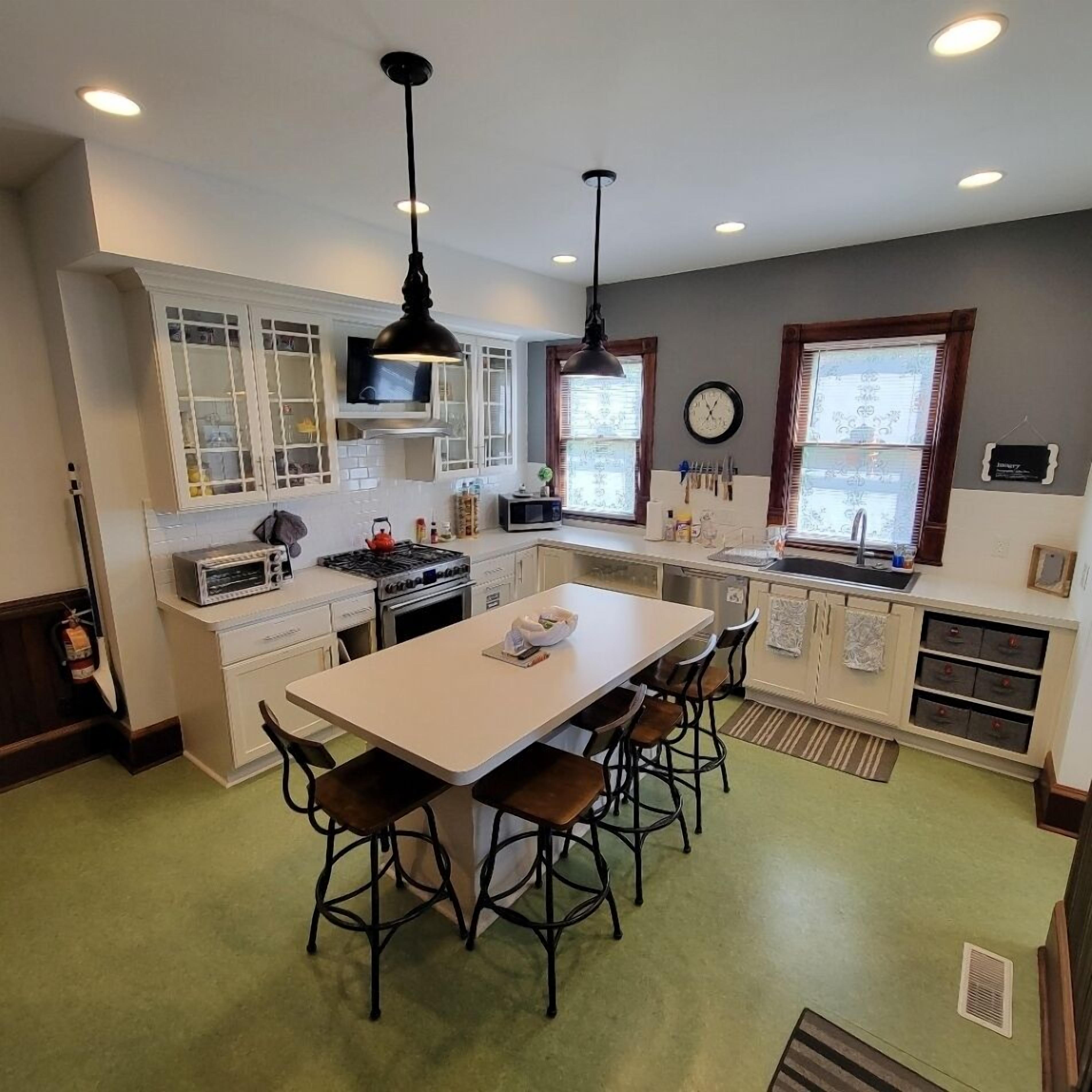 Una cocina moderna con una isla central, armarios blancos y una zona de comedor con taburetes de bar.