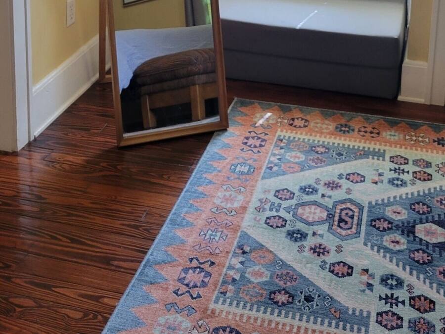 Una habitación con techo inclinado, una ventana con cortinas, un sofá, un espejo y una alfombra estampada.