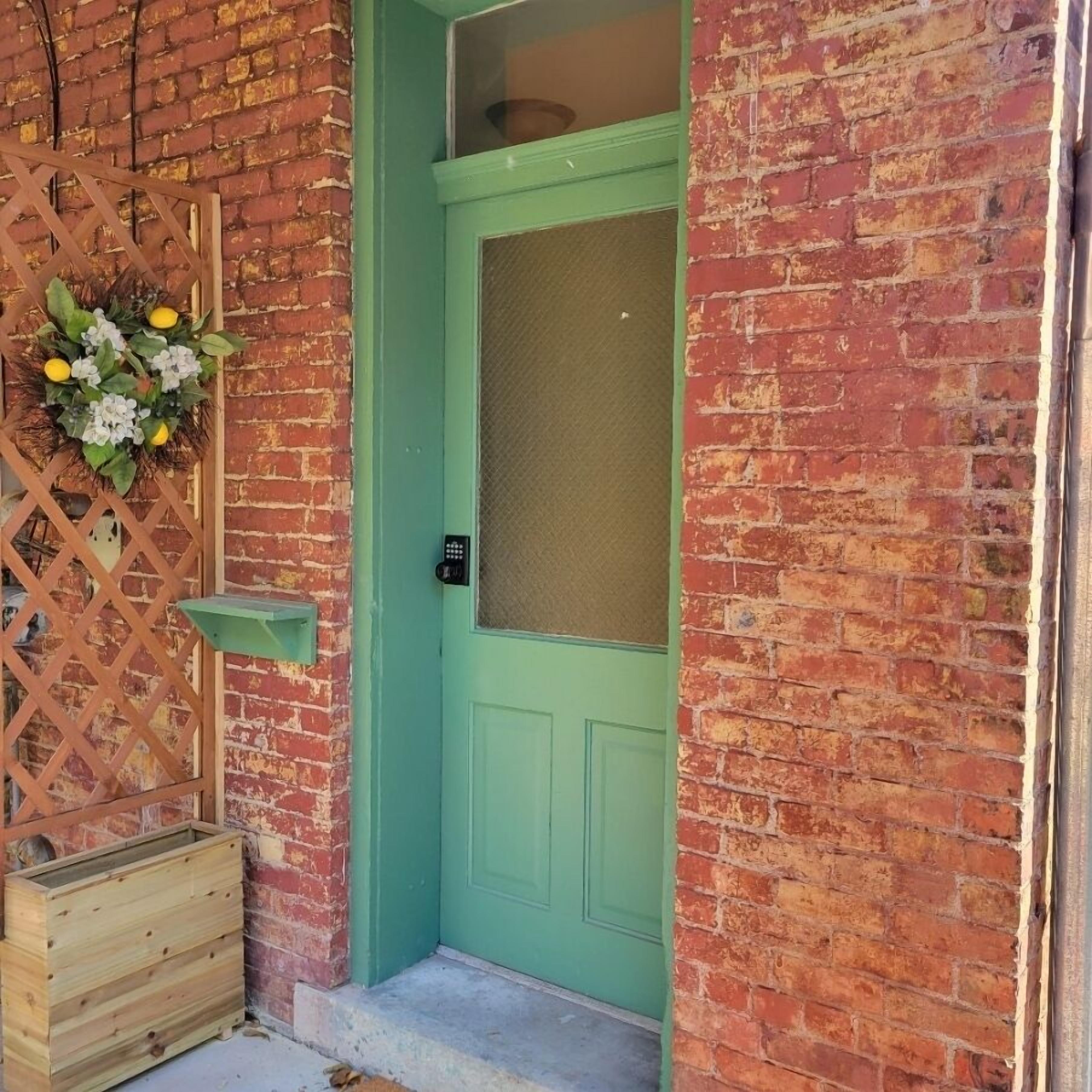 A green door with a small shelf and a wall-mounted wreath.