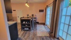 Una cocina moderna con suelo de madera oscura, un comedor con mesa y sillas, y un gran ventanal con cortinas.